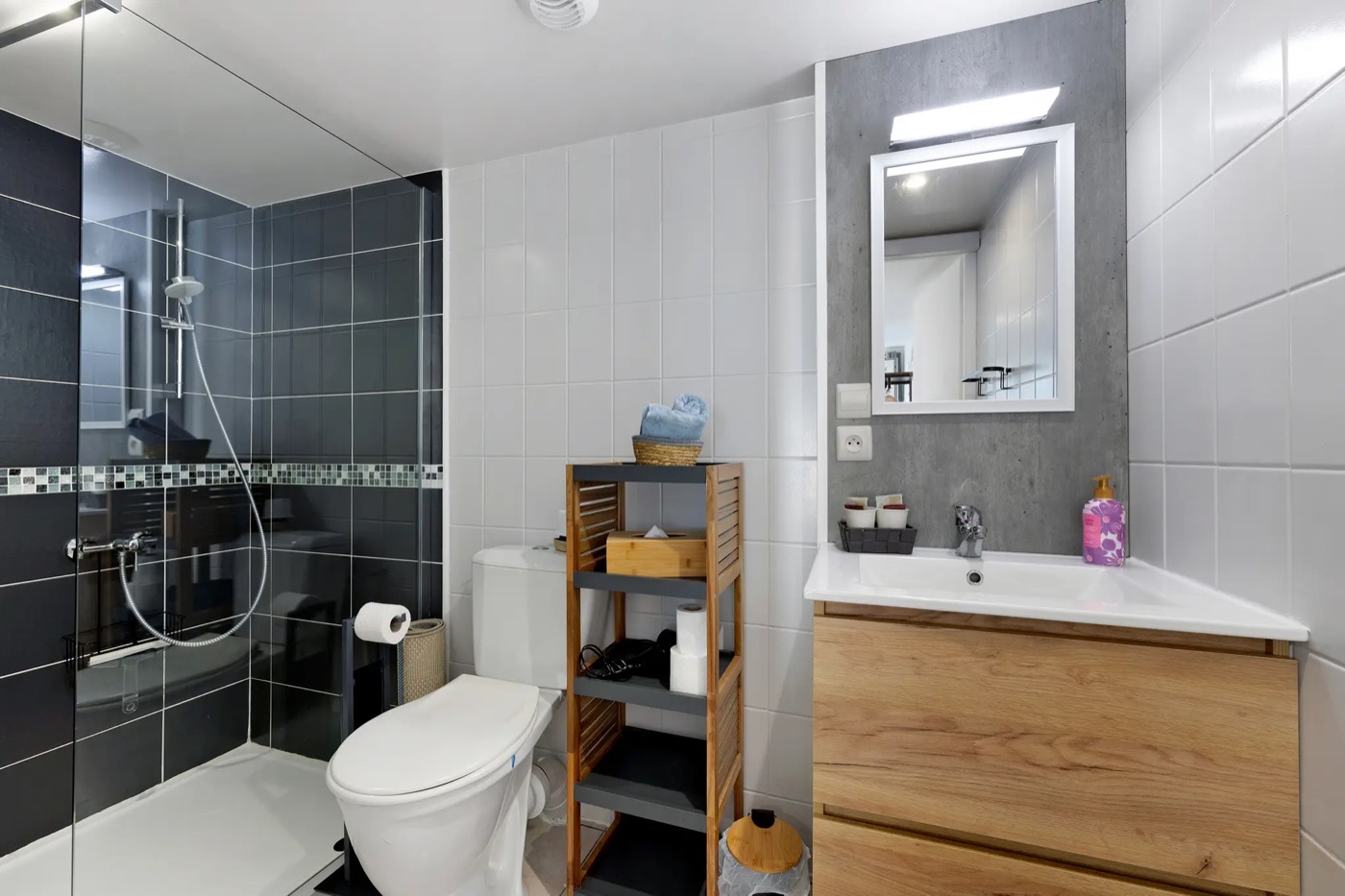 Shower room with dark tiles, a glass shower, a washbasin on a wooden unit and a toilet