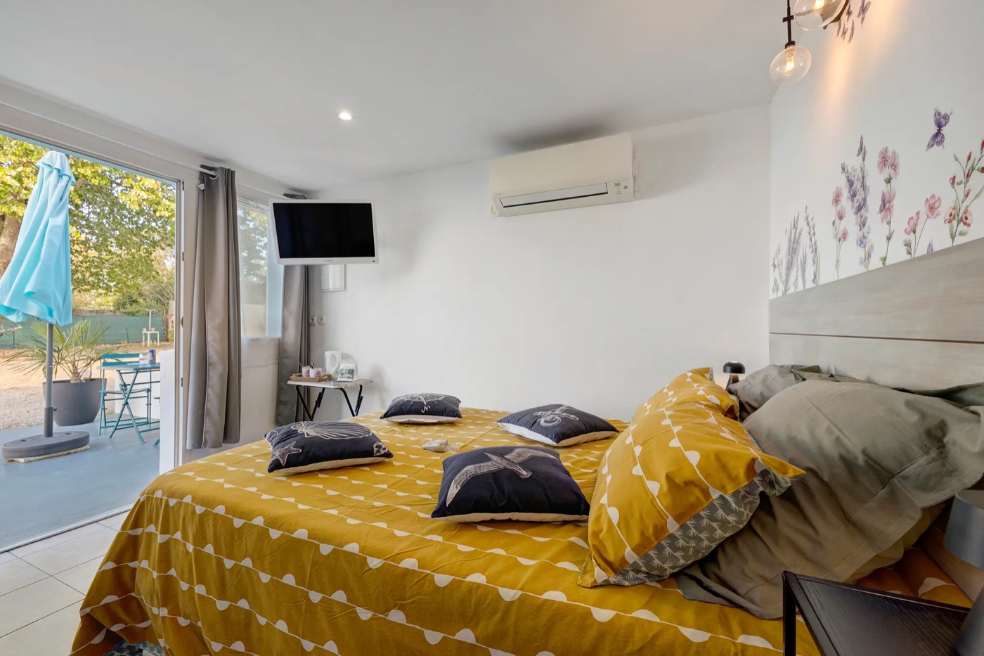 Double room with a yellow bedspread and a patio window opening onto the terrace and its parasol