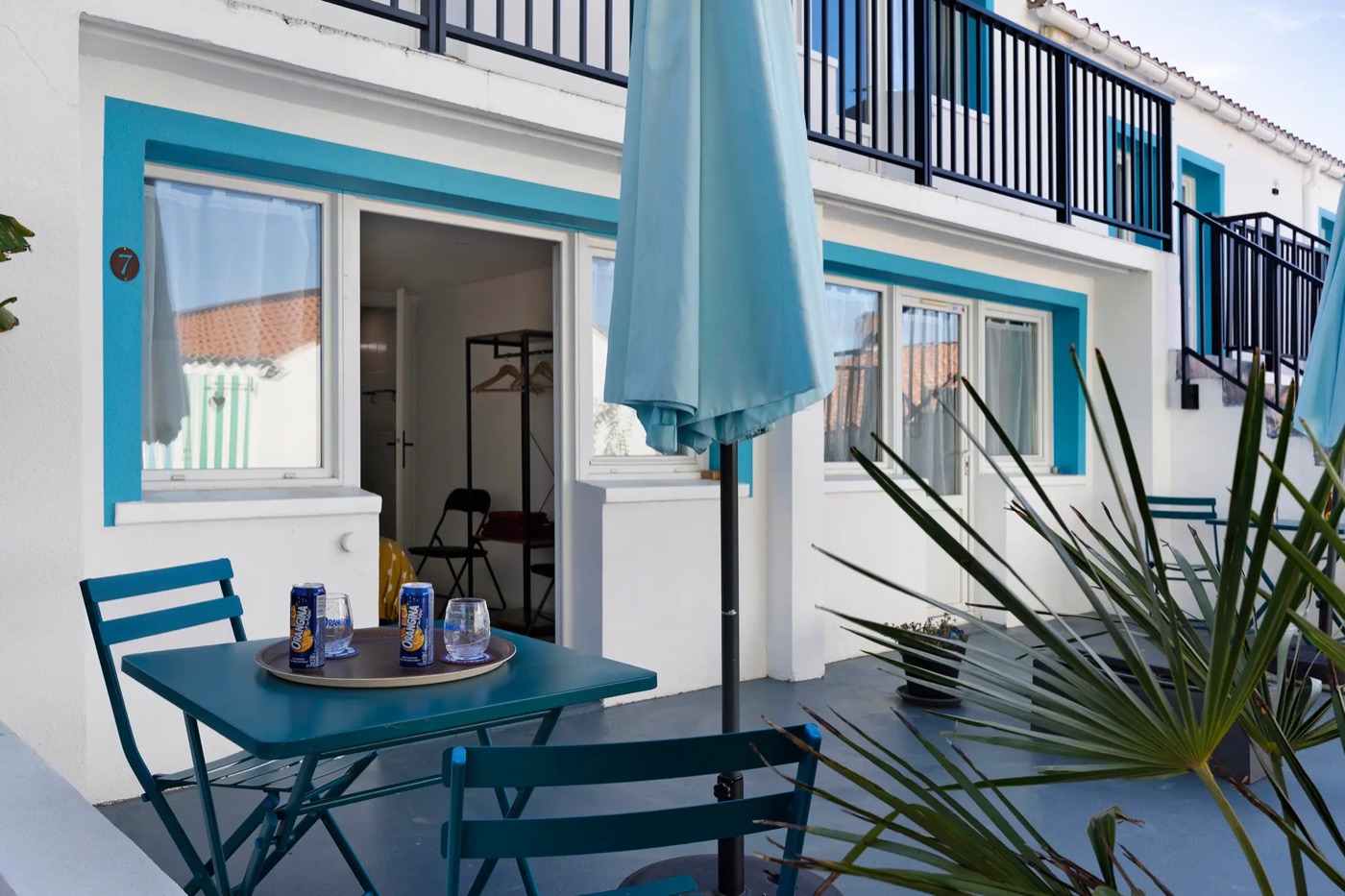 Ground-level terrace outside a room: blue table, chairs and parasol